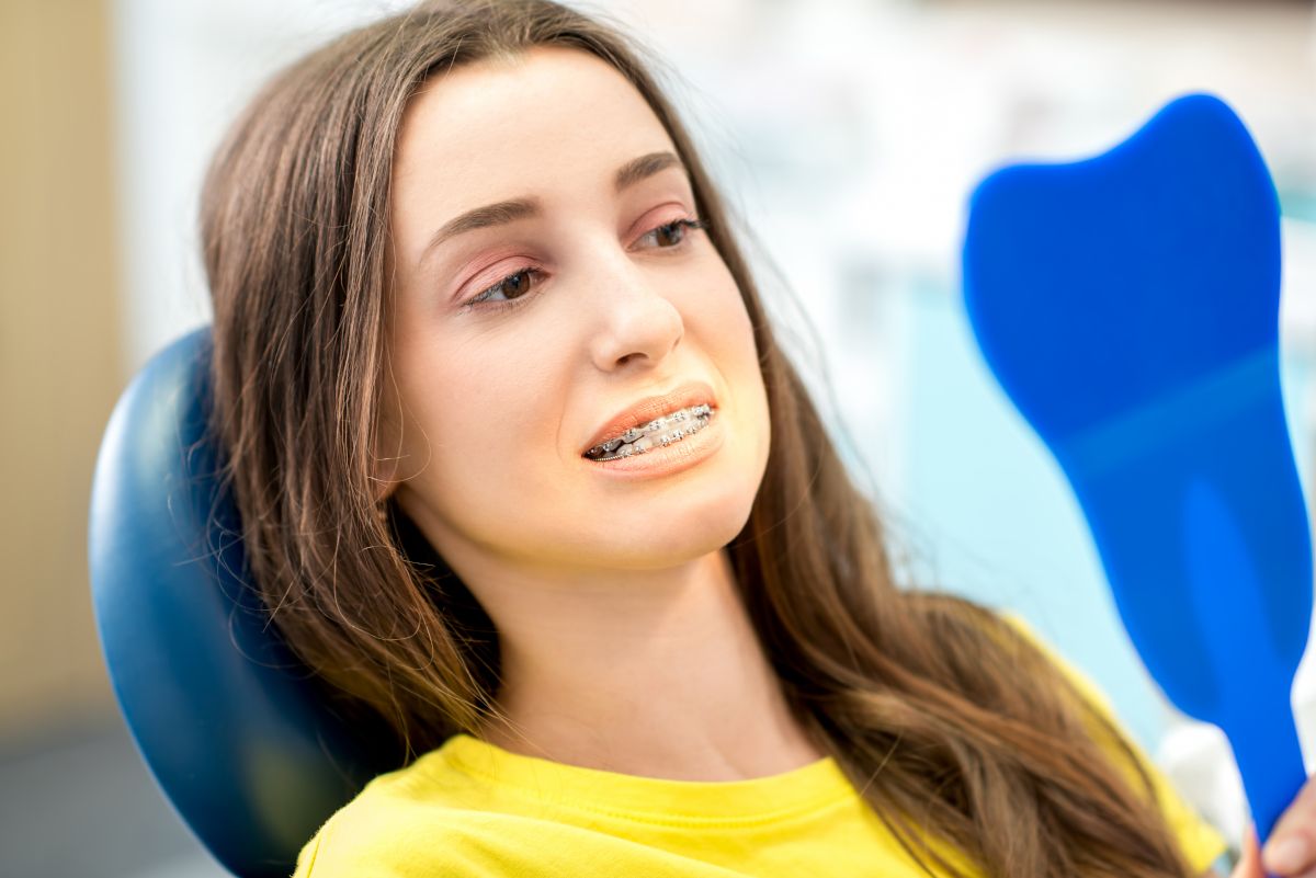 Young woman in yellow shirt smiling in dental office chair during orthodontic appointment.