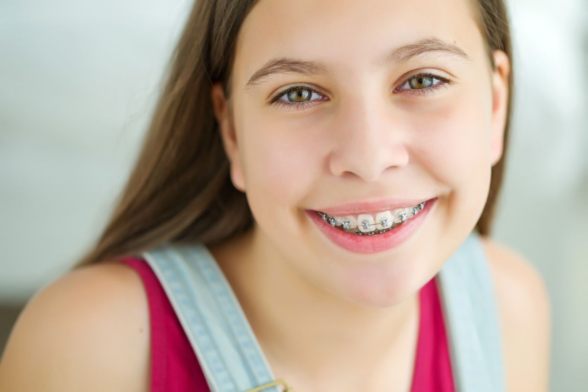 Young girl smiling at camera wearing braces, indoor portrait setting.